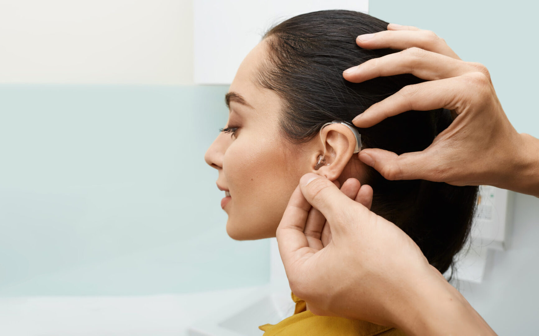 Installation hearing aid on woman's ear at hearing clinic, close-up, side view. Deafness treatment, hearing solutions Installation hearing aid on woman's ear at hearing clinic, close-up, side view. Deafness treatment, hearing solutions